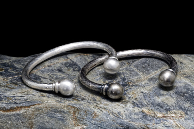 satin Cribbar torque cuff leaning on Oxidised Cribbar cuff